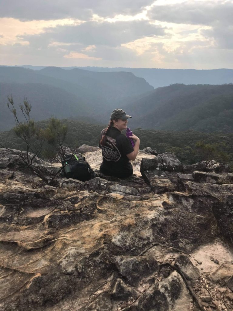 Person sitting on rocky outcrop looking out over valley and mountains on hike to Lockleys Pylon Blue Mountains