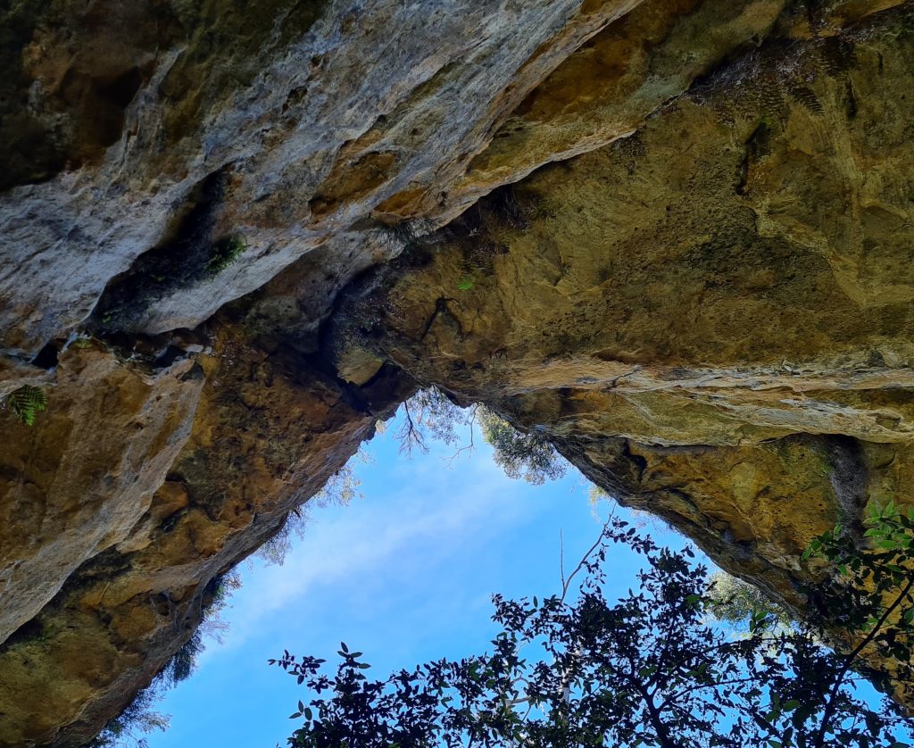 Photo taken looking up at sky beyond roof of Walls Cave. Sky forms a triangle in the centre of the image