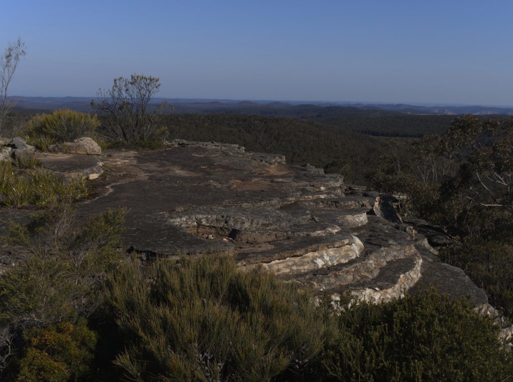 Image is of rock formation on Kings Tableland in the foreground and views south into the Blue Mountains National Park