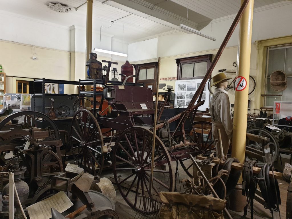 an old horse drawn carriage on display with other exhibits in the Mount Vic Museum in Mount Victoria