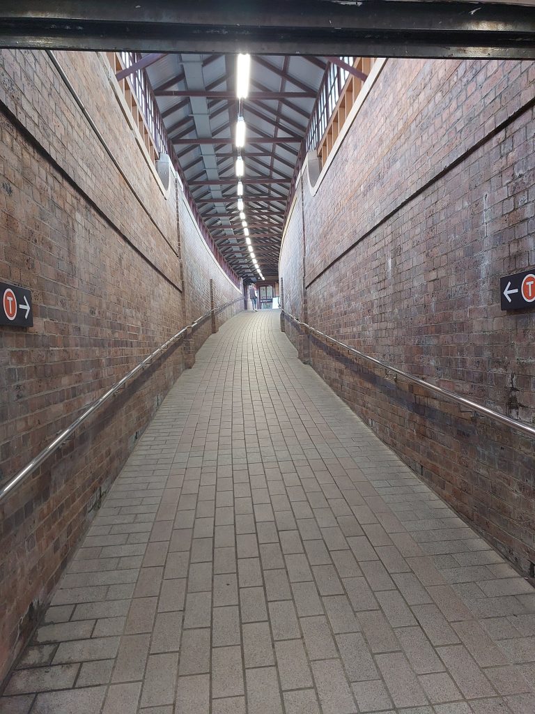 Pictured is the brick walled and tiled floor walkway taking passengers up to the platform at Katoomba Train Station.