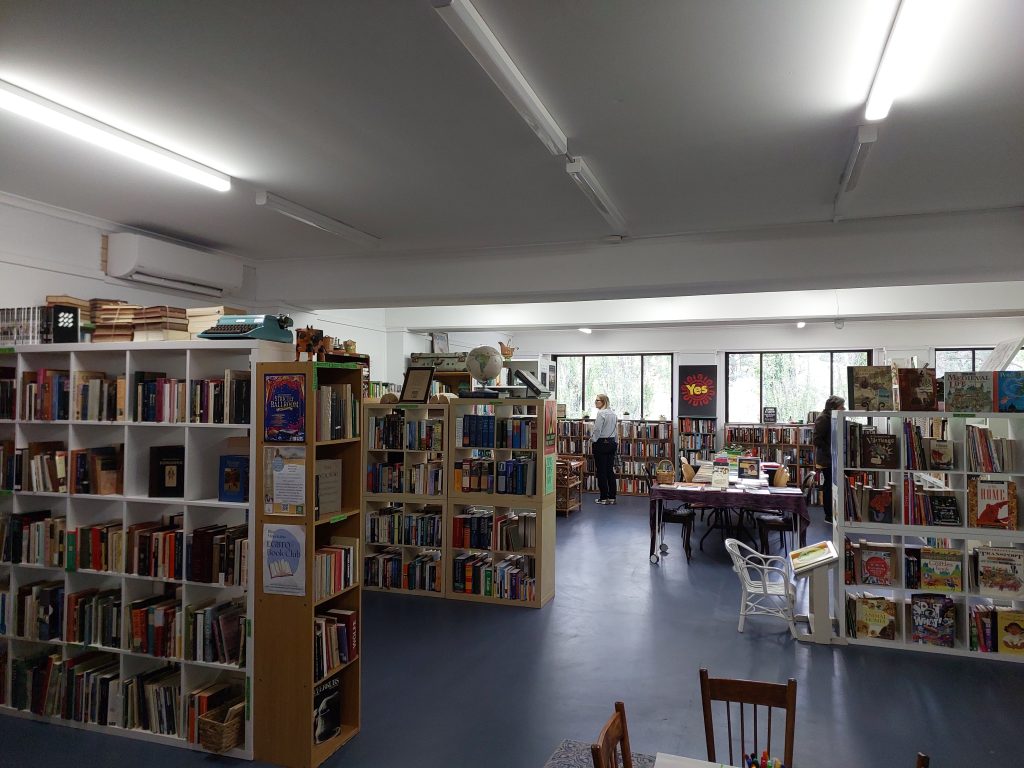 Inside the Good Earth Bookshop in Wentworth Falls. The floor is blue tiles, there are rows of bookshelves and coverless windows at the back of the store filling it with light. 