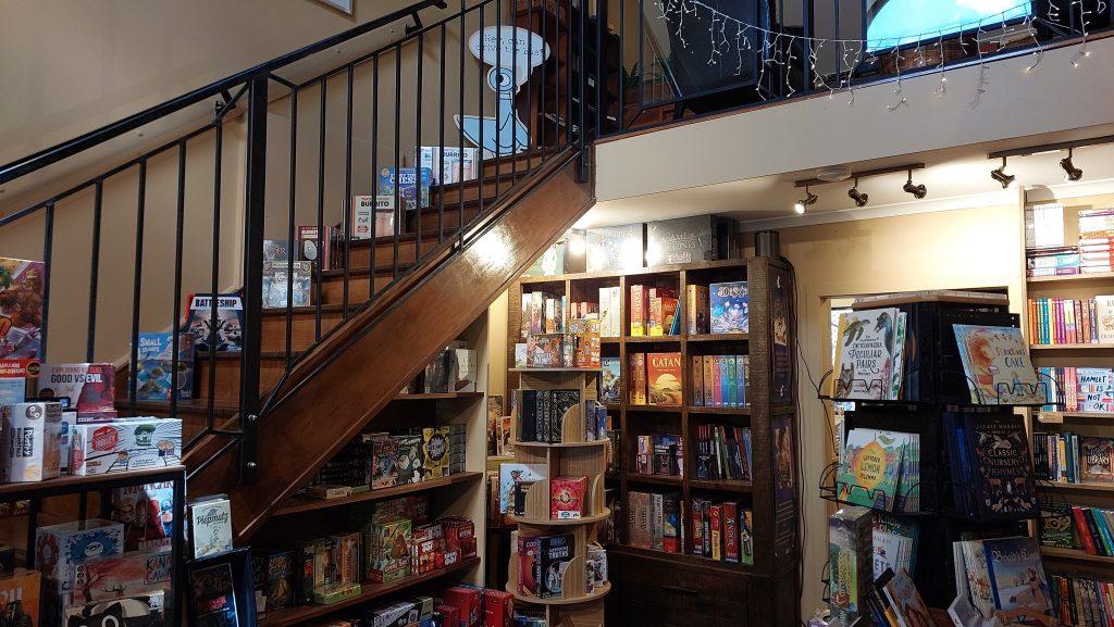 The interior of The Little Lost Bookshop from the front. A set of stairs leads up to a small upper level above the bookshelves